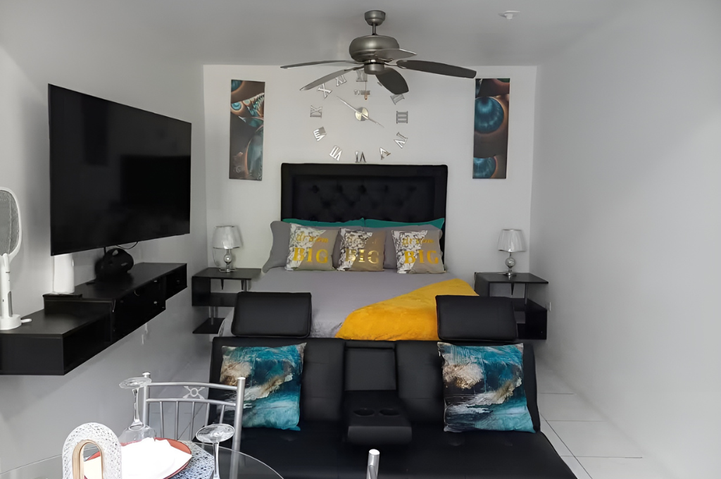 Modern bedroom with queen bed, bold yellow accents, ceiling fan, and wall art at Serenity Zen